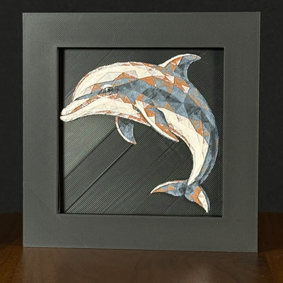 Geometric dolphin framed layered 3D art in Heritage color palette, featuring a leaping dolphin with soft white, gray, black, and neutral brown layered details inside a charcoal matte display frame.