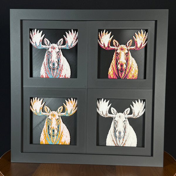 Four-panel framed geometric moose layered art set showing the same front-facing moose portrait in four WTX3D color palettes, arranged in a charcoal black 2x2 frame with large antlers, detailed fur texture, and high-contrast layered color.