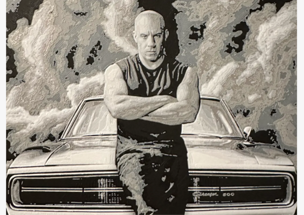 Framed 3D layered art piece featuring a stylized monochrome illustration of a bald action movie hero standing with crossed arms while leaning against the front of a classic muscle car. The background shows dramatic, high-contrast clouds of smoke and textured patterns in a grayscale color scheme.