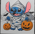 Framed 3D layered art piece featuring a cute illustration of a blue alien character dressed as a mummy wrapped in white bandages, standing between two carved Halloween jack-o'-lantern pumpkins with an ancient Egyptian pyramid and flying bats in the background.