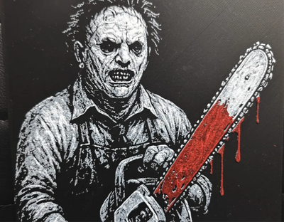Framed 3D layered art piece featuring a detailed grayscale illustration of a classic horror movie slasher wearing a stitched leather mask and holding a chainsaw accented with bright red blood details.