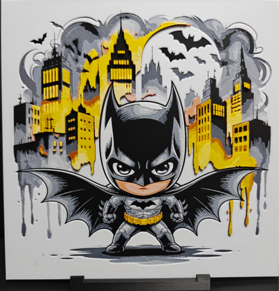 Framed 3D layered art piece featuring a cute chibi illustration of a dark comic book vigilante wearing a black and grey bat suit with a yellow belt and wide spread bat wings, standing fiercely in front of a stylized yellow cityscape with grey clouds, flying bats, and a full moon.
