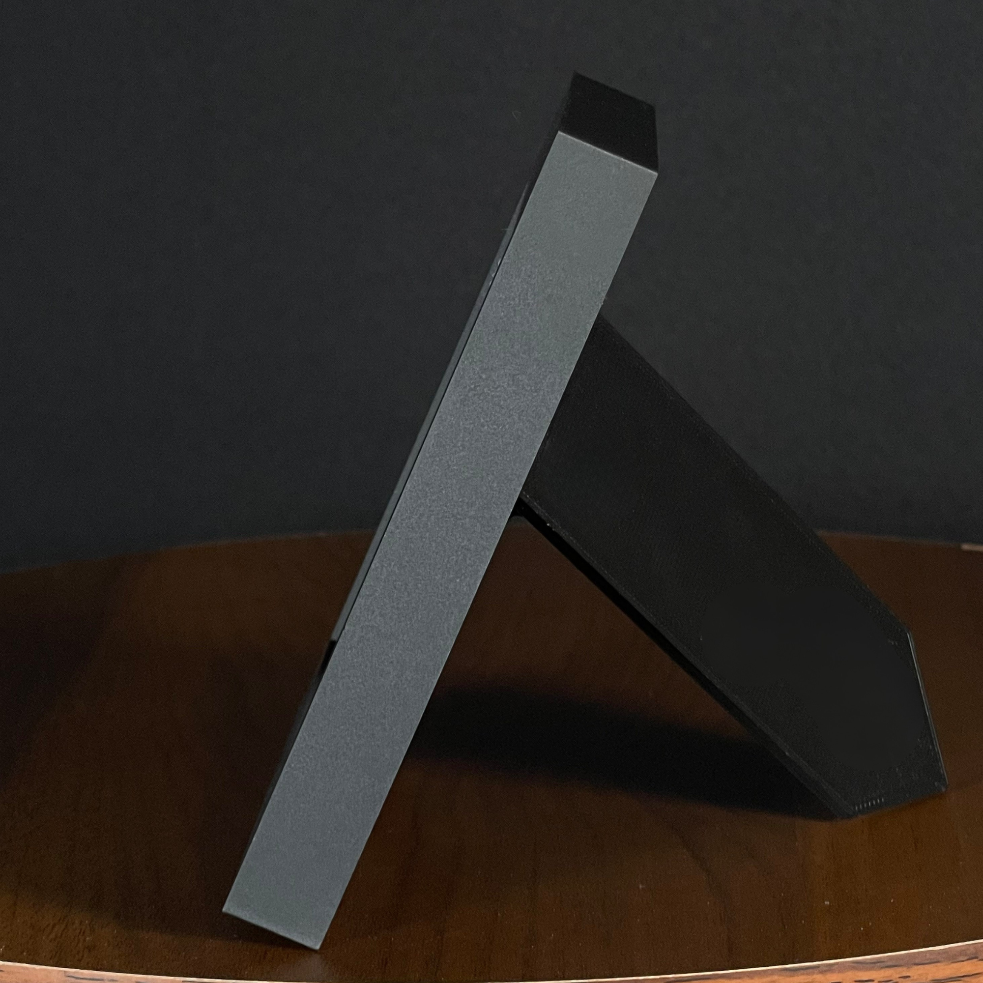 Side view of a WTx3D charcoal matte frame with the built-in easel stand open on a wooden surface.
