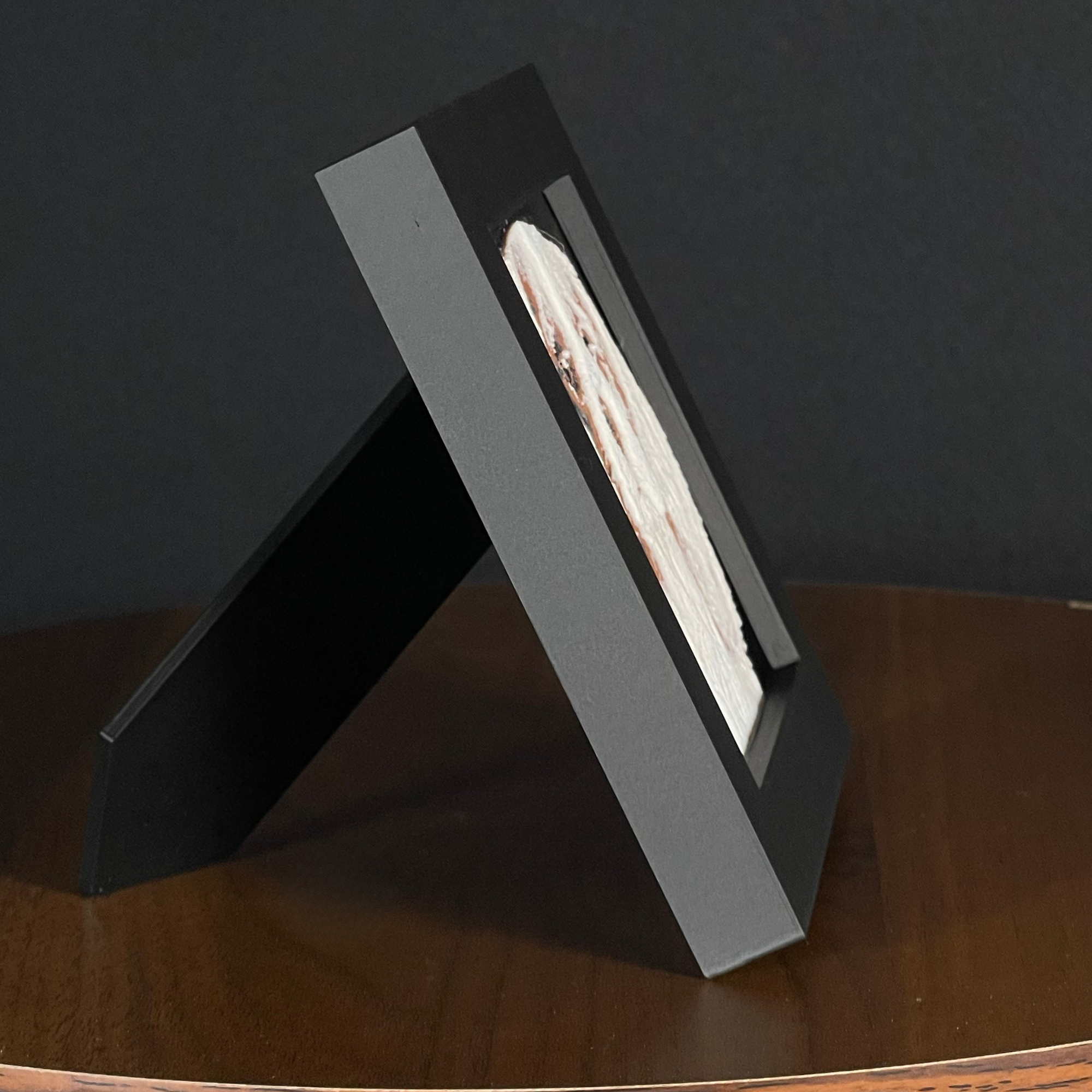 Side of a WTx3D charcoal matte frame with the built-in easel stand open on a wooden surface.