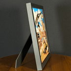 Side view of a WTx3D Large charcoal matte frame with the built-in easel stand open on a wooden surface. Available as Small or Large Framed 3D Layered Art — Large features approximately 8" × 8" artwork in a finished frame measuring approximately 11½" × 11½".
