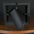 Rear easel view of a WTx3D Small charcoal matte frame with the built-in easel stand open on a wooden surface. Available as Small or Large Framed 3D Layered Art — Small features approximately 4" × 4" artwork in a finished frame measuring approximately 5⅛" × 5⅛".